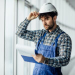 Happy young man architect in hard hat holding folder.