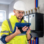 Man, an electrical technician working in a switchboard with fuses, uses a tablet.