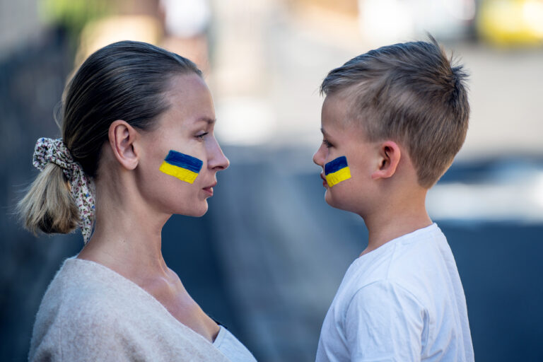 Families against war. Upset Ukrainian boy looking at his mother, with blue yellow flag on his face,  protesting war conflict. Evacuation of civilians. Freedom to Ukraine. Stop Russian aggression.